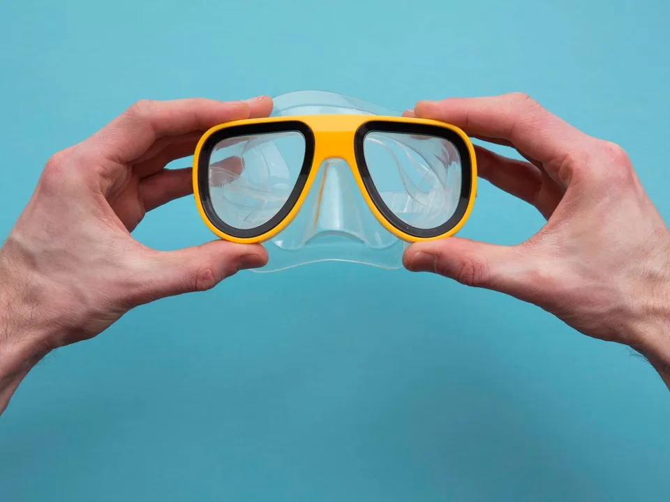 Mains tenant un masque de plongée jaune sur fond bleu